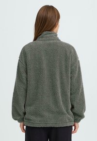 Fleece pullover i mørkegrøn farve med høj krave, drop shoulders og en blød, tekstureret overflade. Detaljerne inkluderer en afslappet pasform og ribbet kant.