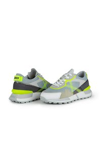 Zapatos deportivos en gris y blanco con materiales de malla y ante, detalles en neón verde, que presentan una suela texturizada y elementos de diseño en contraste.