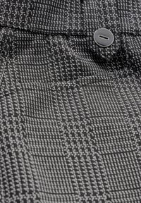 Mustekki ja harmaa ruudullinen kangas, jossa on tekstuurimainen kuvio ja sileä pinta, korostettuna yhdellä harmaalla napilla.