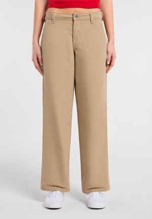 Pantaloni beige a gamba larga con una texture liscia, dotati di chiusura frontale a bottone e tasche laterali, indossati con sneakers bianche.