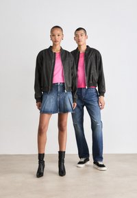 Sorte bomberjakker med lynlås foran, lyserøde t-shirts, denimskørt, slidte jeans og sorte ankelstøvler; minimalistisk design og farvekontrast.
