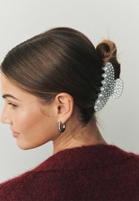 Silberner Haarklammer in Form eines Schmetterlings, geschmückt mit Strasssteinen, der einen tiefen Dutt hält. Schwarz strukturierter Pullover im Hintergrund sichtbar.