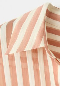 Chemise à col avec larges rayures verticales alternant des couleurs pêche douces et blanc cassé, montrant une texture de tissu détaillée et des coutures apparentes.