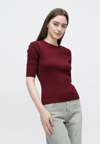 Vinrød, kortermet tettsittende topp med rund hals, ribbet tekstur og sømløse skuldre, kombinert med lysegrå jeans.