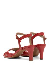 Czerwone skórzane sandały na wysokim obcasie z krzyżującymi się paskami, ozdobami na klamry i zwężanym obcasem. Miękka podszewka wewnętrzna, gładka tekstura.