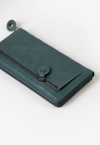 Portafoglio in pelle verde acqua con chiusura a zip e bottone a pressione. Presenta una texture liscia e un dettaglio in metallo della zip a contrasto.