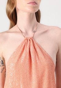 Halter neck topp i lys fersken, dekket med paljetter for tekstur. Har et samlet design ved utringningen og en slank stropp.