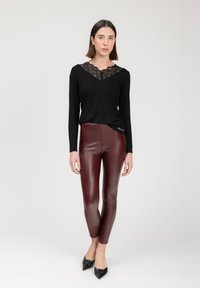 Schwarzes Langarmoberteil mit Spitzenverzierungen am Kragen, kombiniert mit burgunderfarbenen High-Waist-Leggings und schwarzen spitzen Schuhen.