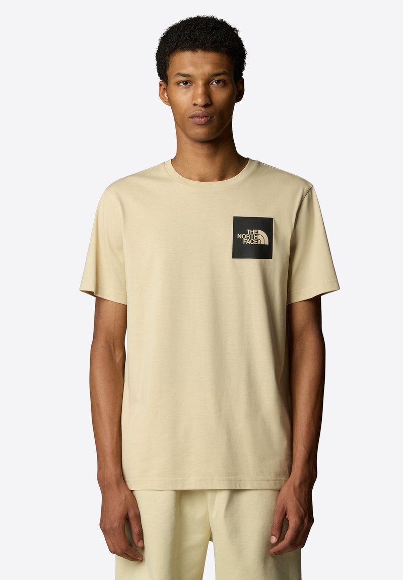 Beige bavlněné tričko s kulatým výstřihem, krátkými rukávy a černým čtvercovým logem na levém hrudníku s nápisem "THE NORTH FACE."