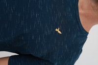 Άνδρας που φοράει μπλε ναυτικό κοντομάνικο με υφή και μια μικρή κίτρινη κεντημένη μέλισσα στο στήθος, εμφανιζόμενος από τον ώμο και πάνω.