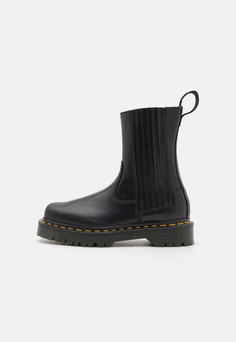 Bottine en cuir noir avec panneaux élastiques, coutures jaunes et semelle robuste. Comprend une languette pour un enfilage facile.