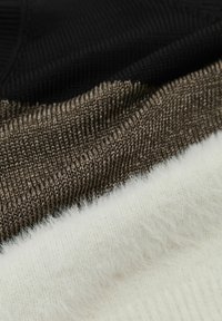 Kootud kangas mustas, pruunis ja valges; valge osa on pehme ja koheline tekstuur, samas kui teised on tihedamad ja siledamad.