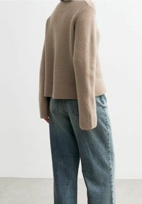 Vaalean beige värinen ribbiknitti neule, jossa on rento istuvuus, korkea kaula-aukko ja hieman levenevät hihat, yhdistettynä vaaleansinisiin korkeavyötäröisiin farkkuihin.