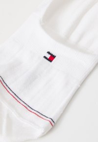 Meia de algodão branca com um pequeno logotipo em vermelho e azul. Realçada com riscas vermelhas e azuis ao longo da borda superior. Textura canelada subtil.