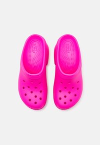 Roza plastična obutev s perforiranimi luknjami, zaobljenim prstom in gladko strukturo. Oblazinjen podplat z oznako "CROCS COMFORT".