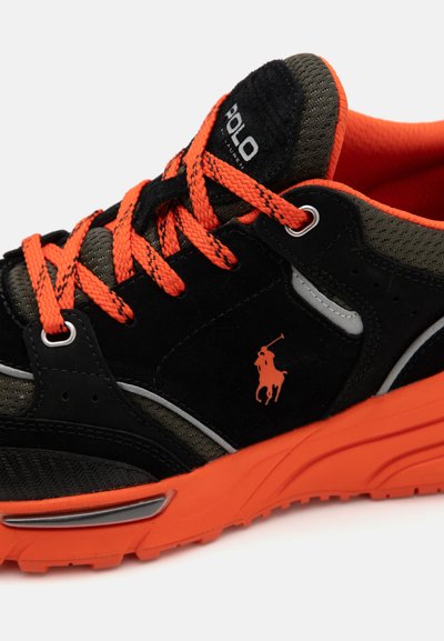 Schwarze und orange Sneaker verfügen über ein Obermaterial aus Wildleder und Mesh, eine runde Zehenpartie, eine strukturierte Sohle und ein markantes Logo an der Seite.