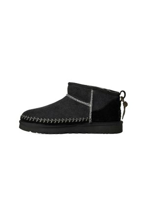 Pantofole nere fino alla caviglia con cuciture bianche visibili, suola piatta, tomaia in tessuto morbido e anello con cordino annodato sul tallone.
