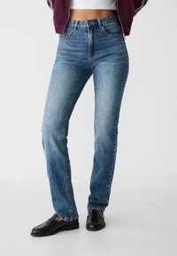 Höga, raka jeans i ljusblå denim med blekta accenter. Har en klassisk femficksdesign och metallknäppning.