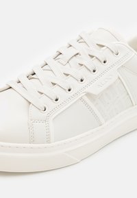 Hvite lær sneakers med flate snøringer, teksturert sidepanel og pregede logo-detaljer. Rund tå og gummisåle for godt grep.