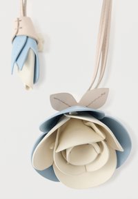 Pandantiv din piele în formă de floare, cu petale suprapuse în nuanțe de albastru deschis și crem, având o curea bej și un accent în formă de frunză.