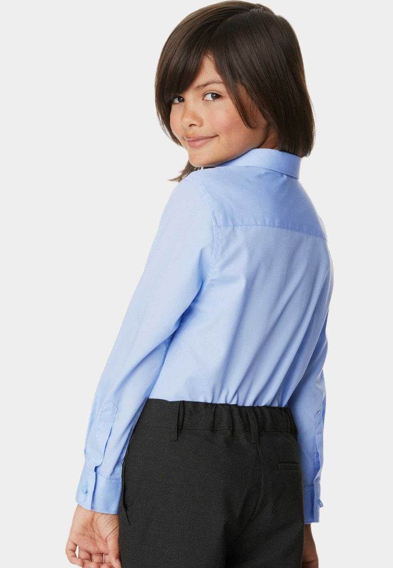 Camicia azzurro chiaro con colletto, maniche lunghe e polsini bottonati; abbinata a pantaloni scuri con una cintura elasticizzata.