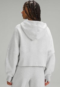 Krossad grå hoodie i mjukt tyg med huva, låga axlar och subtil sömdetaljering. Har logotyp på baksidan.