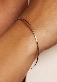 Thin gold bangle bracelet on a wrist, featuring a smooth, shiny finish and a minimalist design with no additional accents or patterns.