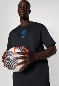 Sort bomulds t-shirt med et blåt Inter Milan logo og Nike swoosh, holdt med begge hænder på en sort-hvid mønstret fodbold.
