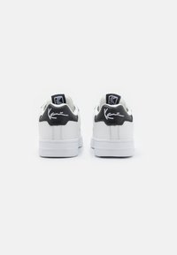 Hvide sneakers med sorte læderdetaljer, der har en glat overflade, rund tå og et signaturlogo på hælen. Tykk hvid sål.