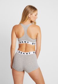 Sport bra DKNY grigio con design a sostegno incrociato e band bianca a contrasto con scritte nere, abbinato a pantaloni corti grigi coordinati.