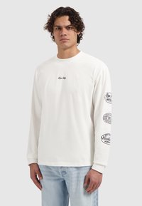 Wit T-shirt met lange mouwen van katoen, voorzien van een klein logo op de borst en grafische prints op beide mouwen. Losse pasvorm en een ronde hals.