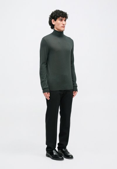 Temnozeleni pulover s turtleneck ovratnikom, v kombinaciji s črnimi hlačami in črnimi čevlji. Pulover ima dolge rokave in prilagojeno obliko.