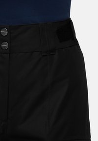 Pantalon noir avec une texture lisse, deux boutons en argent portant la mention "MAMMUT", et une sangle en Velcro à la taille pour un ajustement réglable.