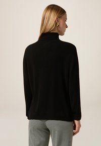 Maglione a collo alto nero in materiale morbido, con una vestibilità rilassata e maniche lunghe. Indossato con pantaloni a motivo houndstooth.
