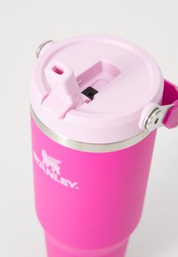 Svetlo roza nerjaveči jekleni potovalni tumbler z svetlo roza pokrovom na preklop in logotipom Stanley na strani.
