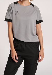 Harmaa urheilupaita mustilla yksityiskohdilla, jossa on pyöreä pääntie, lyhyet hihat ja logo, yhdistettynä mustiin joustohousuihin.