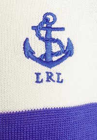 Vitt stickat tyg med en blå broderad ankardesign, med "LRL" nedanför. Randig blå accent i nederkanten.