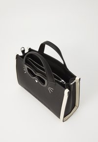 Borsa nera a texture con design di faccia di gatto, caratterizzata da un manico nero lucido, dettagli color crema e un compartimento interno con zip.