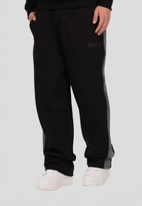 Czarne spodnie dresowe wykonane z miękkiej tkaniny, z elastycznym pasem, bocznymi kieszeniami oraz kontrastowymi szarymi panelami wzdłuż szwów.