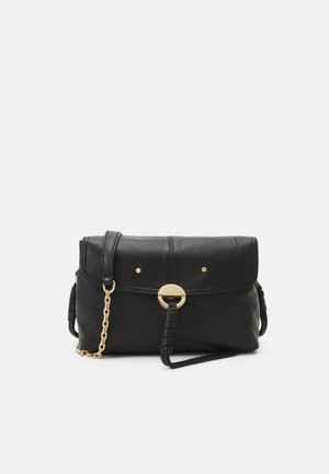 Sac à épaule en cuir noir avec détail chaîne dorée et fermoir rond doré sur le rabat avant sur fond uni.