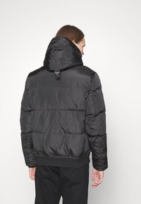 Svart puffjacka med huva, i quiltat material, med elastiska ärmslut och dragsko i halsen för justerbar passform.