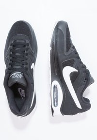 Zwarte atletische sneakers met een bovenwerk van mesh en leer, met witte accenten, een gevoerde schacht en een zichtbare luchtunit in de zool.
