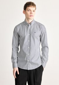 Ελαφρύ πουκάμισο με στενές μπλε και λευκές ρίγες. Διαθέτει μυτερό γιακά και μανίκια με μανσέτες. Κέντημα με λογότυπο στο στήθος.