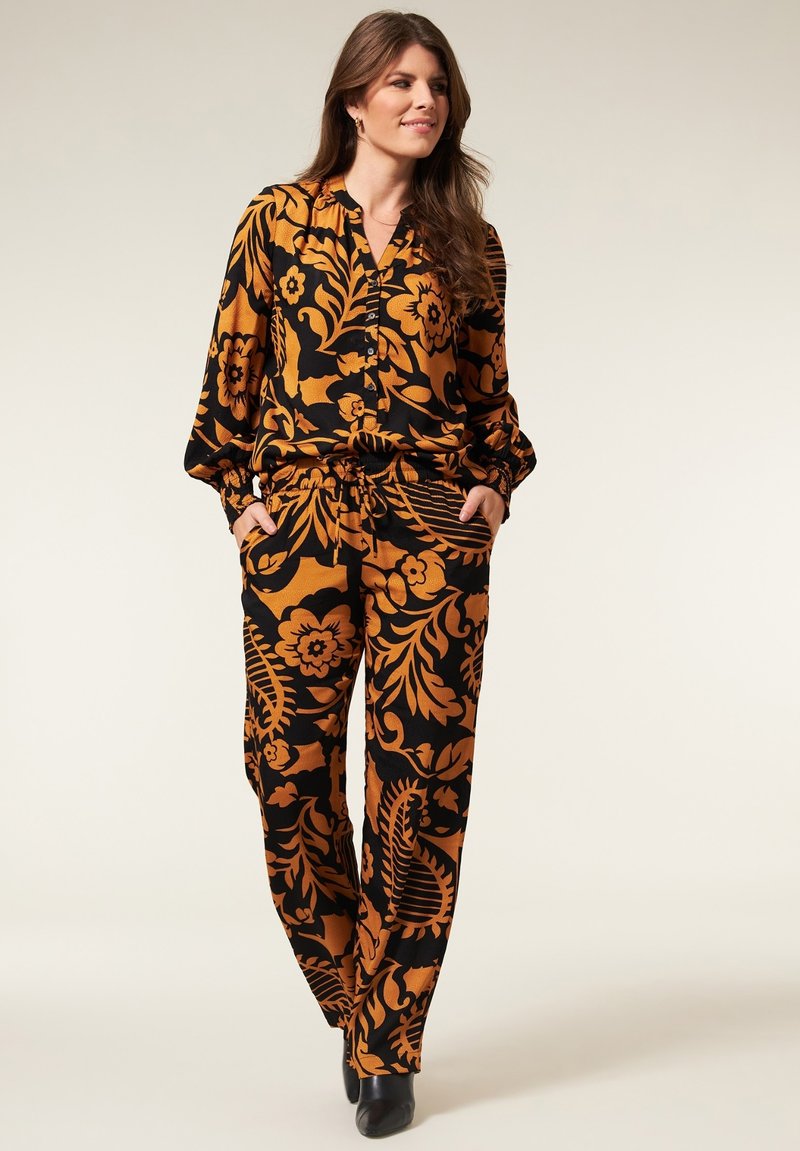 Geprinte blouse en broek set in zwart en oranje bloemenpatroon, met een relaxed fit, knoopsluiting aan de voorkant en zakken.