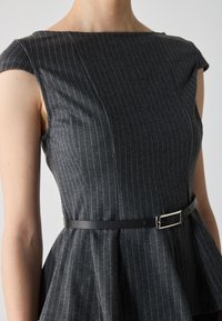 Šedý pruhovaný peplum top s lodičkovým výstrihom, krátkymi rukávmi a čiernym opaskom s obdĺžnikovou striebornou sponou.