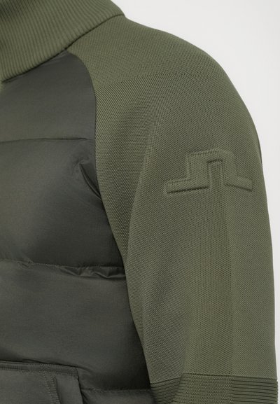 Olive green puffer jacket with textured knit sleeves and embossed geometric logo on upper arm.