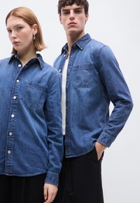 Jeans srajce v modri barvi z zapiranjem na gumbe, ovratnikom, enim žepom na prsih in dolgimi rokavi. Gladko teksturo z enakomernim zaključkom.