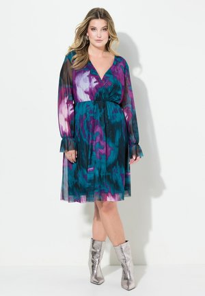 Ärmelloses Kleid mit Gleitaufschlägen in einem Teal-, Lila- und Pink-Ombre-Muster; tailliert; leichtes, durchsichtiges Material; kombiniert mit metallic-silbernen Knöchelstiefeln.