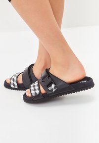 Schwarze Sandalen mit geometrischen grauen Akzenten, verstellbaren Riemen, strukturiertem Fußbett und einer geriffelten Sohle für besseren Halt.