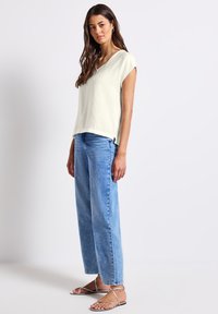 Hellgrünes, strukturiertes Kurzarmoberteil mit einem V-Ausschnitt, kombiniert mit blauen, hoch taillierten, geraden Jeans und flachen silbernen Sandalen.